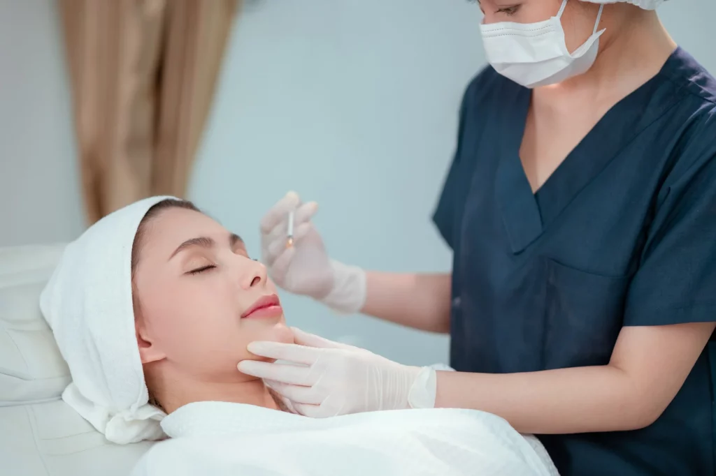 Patient receiving neurotoxin therapy injection in the chin area by a healthcare professional in protective gear for wrinkle reduction.